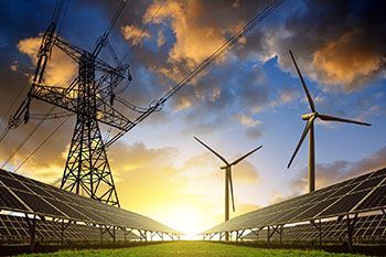Ein Feld aus Solarmodulen und Windturbinen mit Stromleitungen im Hintergrund bei Sonnenuntergang.