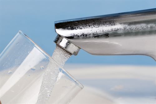 Aus einem Wasserhahn wird Wasser in ein Glas gegossen.