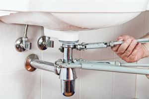 Eine Person repariert ein Waschbecken mit einem Schraubenschlüssel.