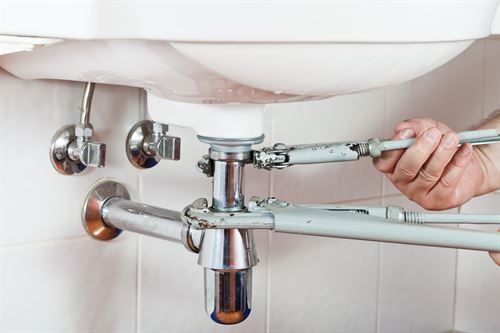 Eine Person repariert ein Waschbecken mit einem Schraubenschlüssel.