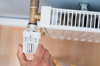 Eine Person stellt einen Thermostat an einem Heizkörper ein