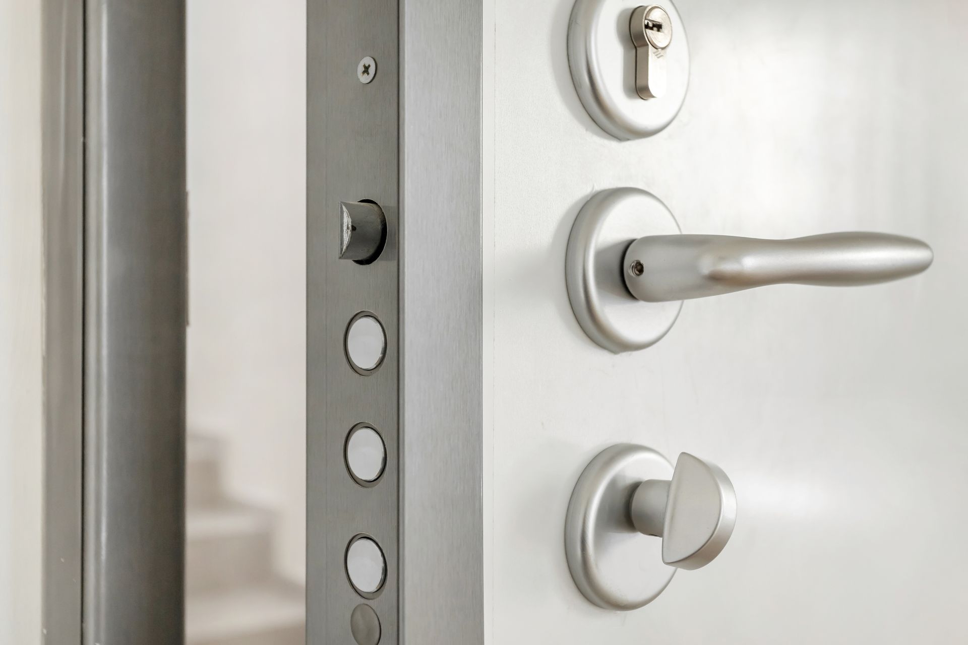 Primer plano de una puerta blanca moderna con herrajes plateados, que incluyen cerradura, manija y cerrojos de seguridad.