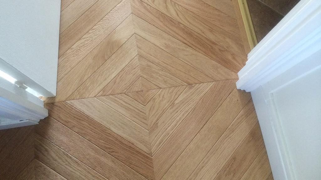 Parquet en bois brun clair à chevrons, visible entre deux encadrements de porte blancs.