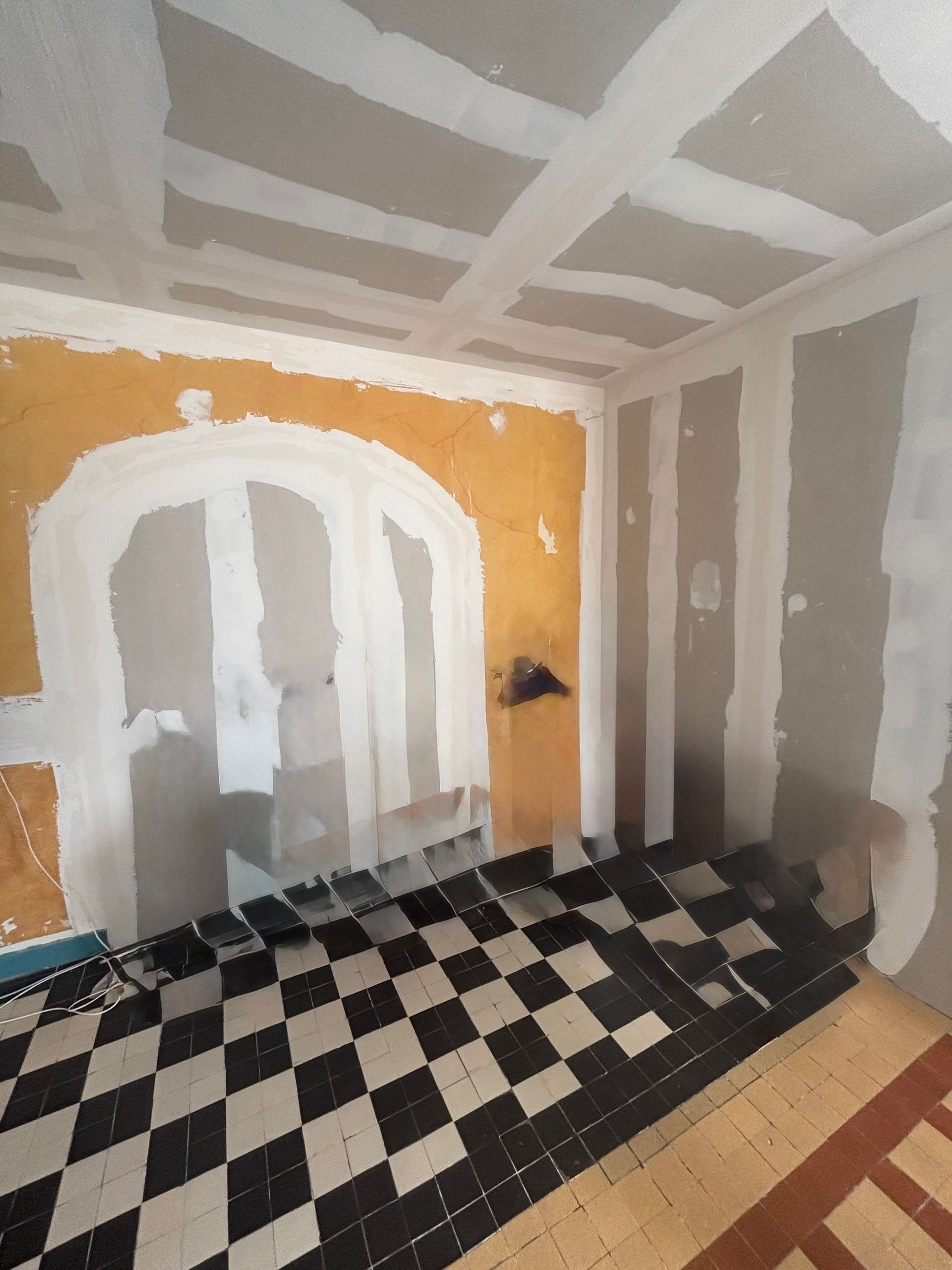 Chambre en rénovation avec sol à damier et murs partiellement enduits.