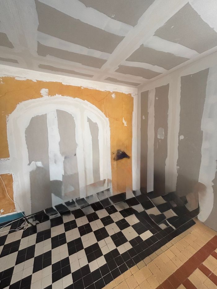 Chambre en rénovation avec sol à damier et murs partiellement enduits.