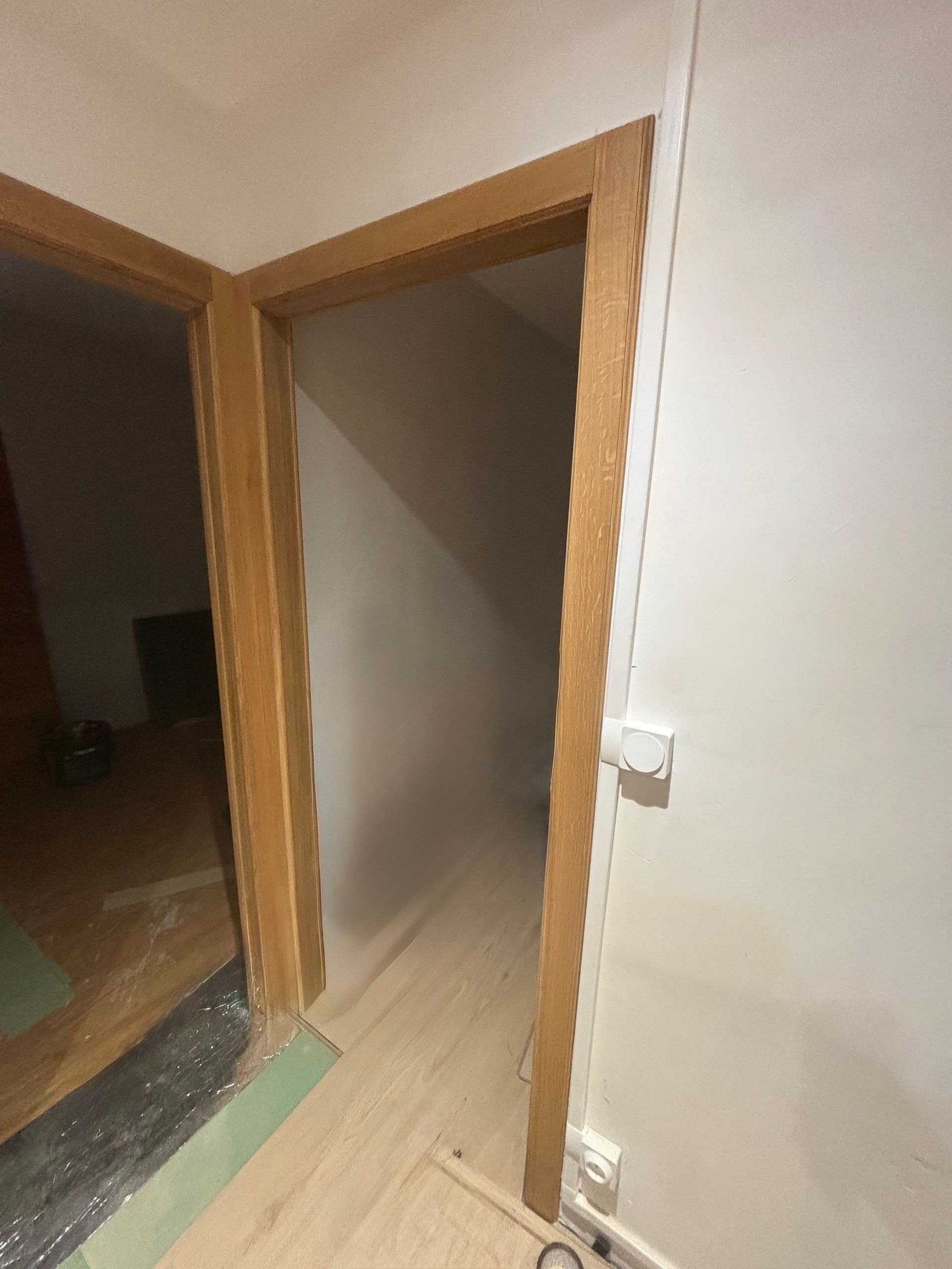 Deux portes aux encadrements en bois clair sur des murs blancs. L'une mène à une pièce, l'autre à un espace mansardé.