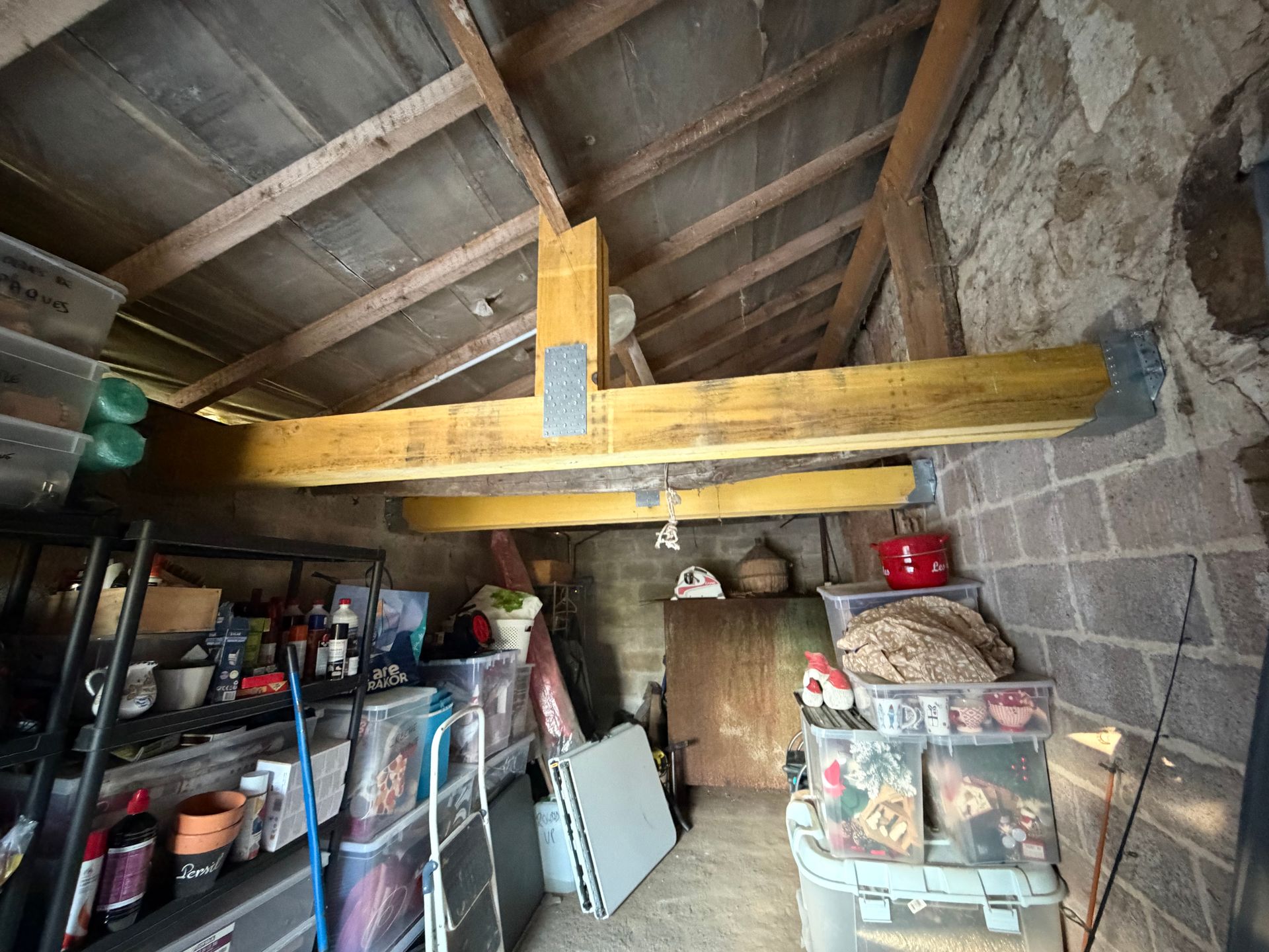 Espace de stockage avec poutres en bois, murs en briques et divers objets dans des bacs et sur des étagères.