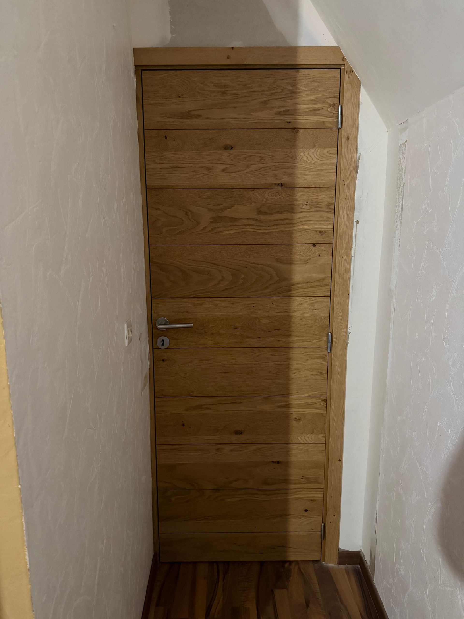 Porte en bois dans un couloir étroit aux murs blancs et au sol en bois.