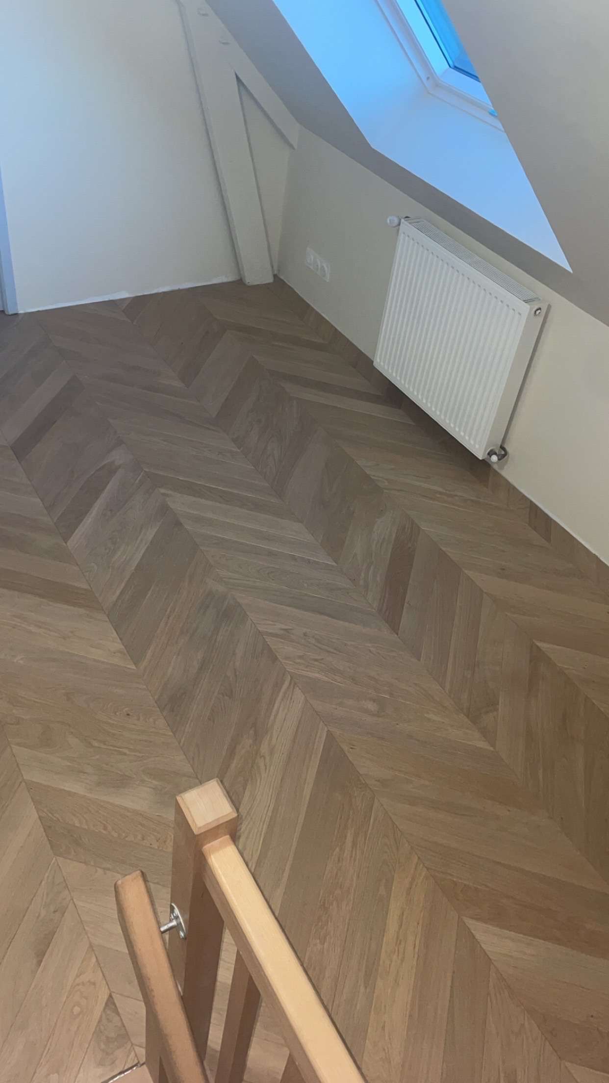 Parquet à chevrons dans une chambre mansardée, avec radiateur et puits de lumière.