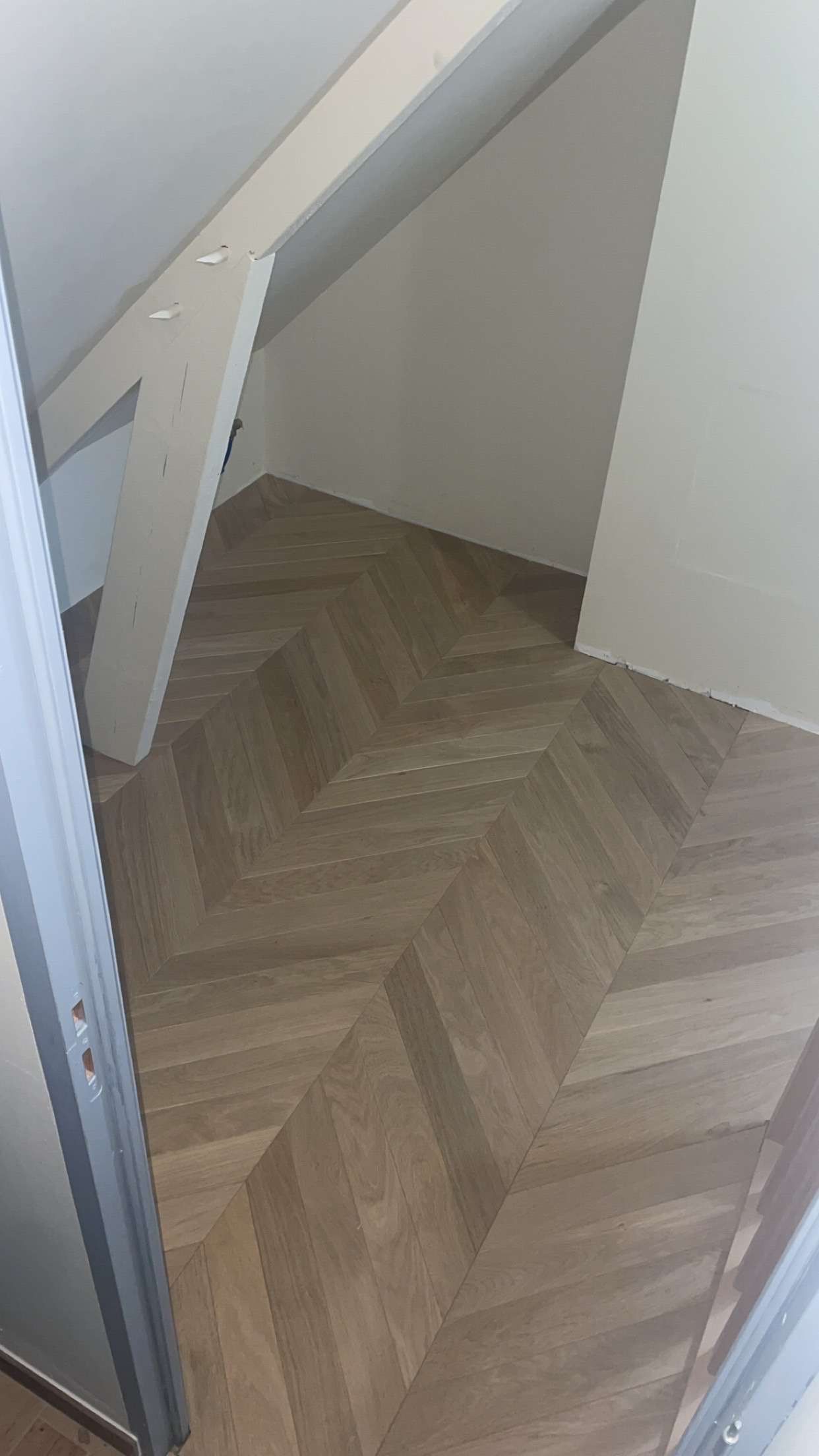 Parquet à chevrons dans une petite pièce aux murs en biais et à la poutre blanche.