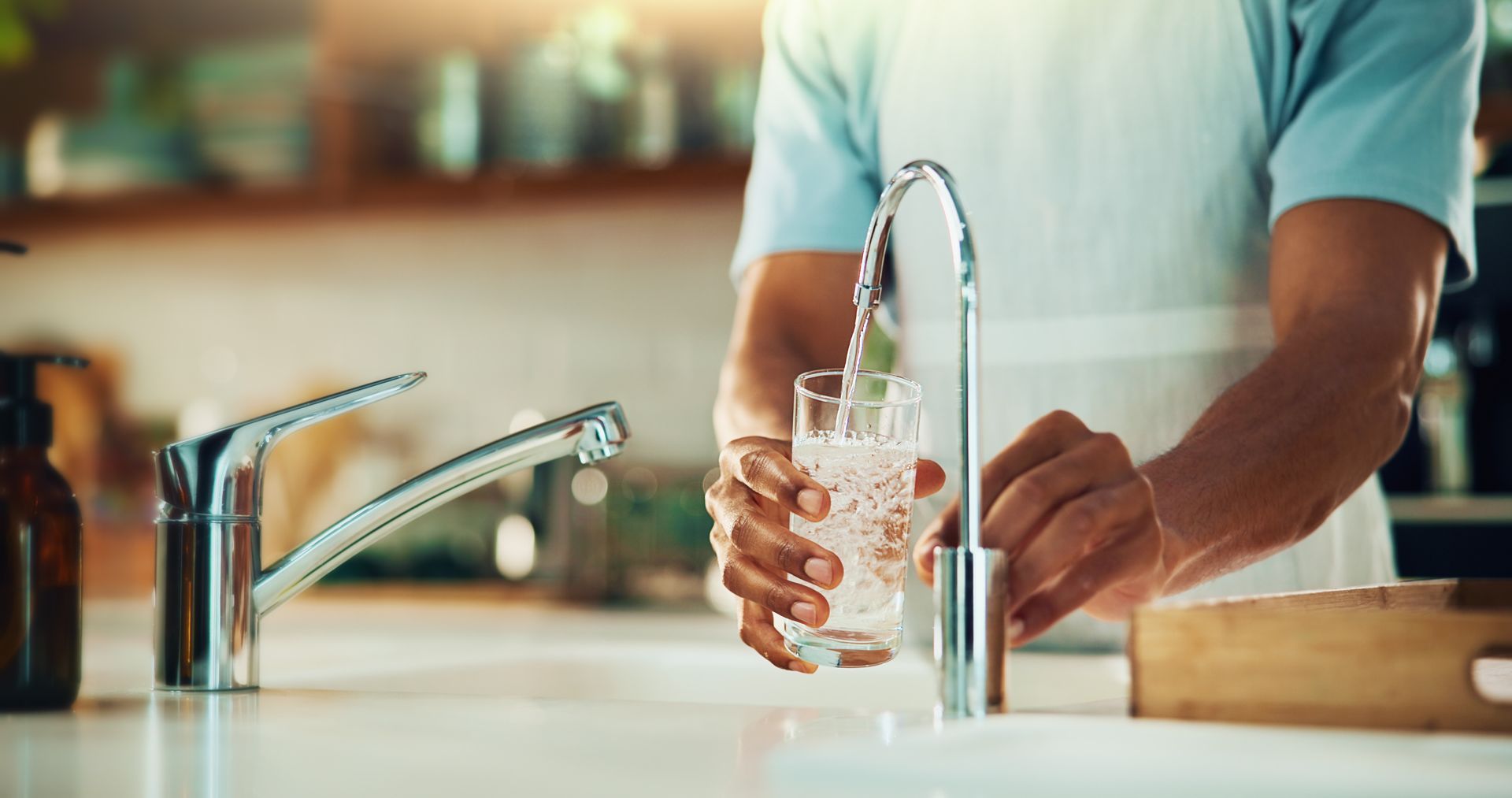 Une personne lave un verre sous le robinet d'eau courante de la cuisine