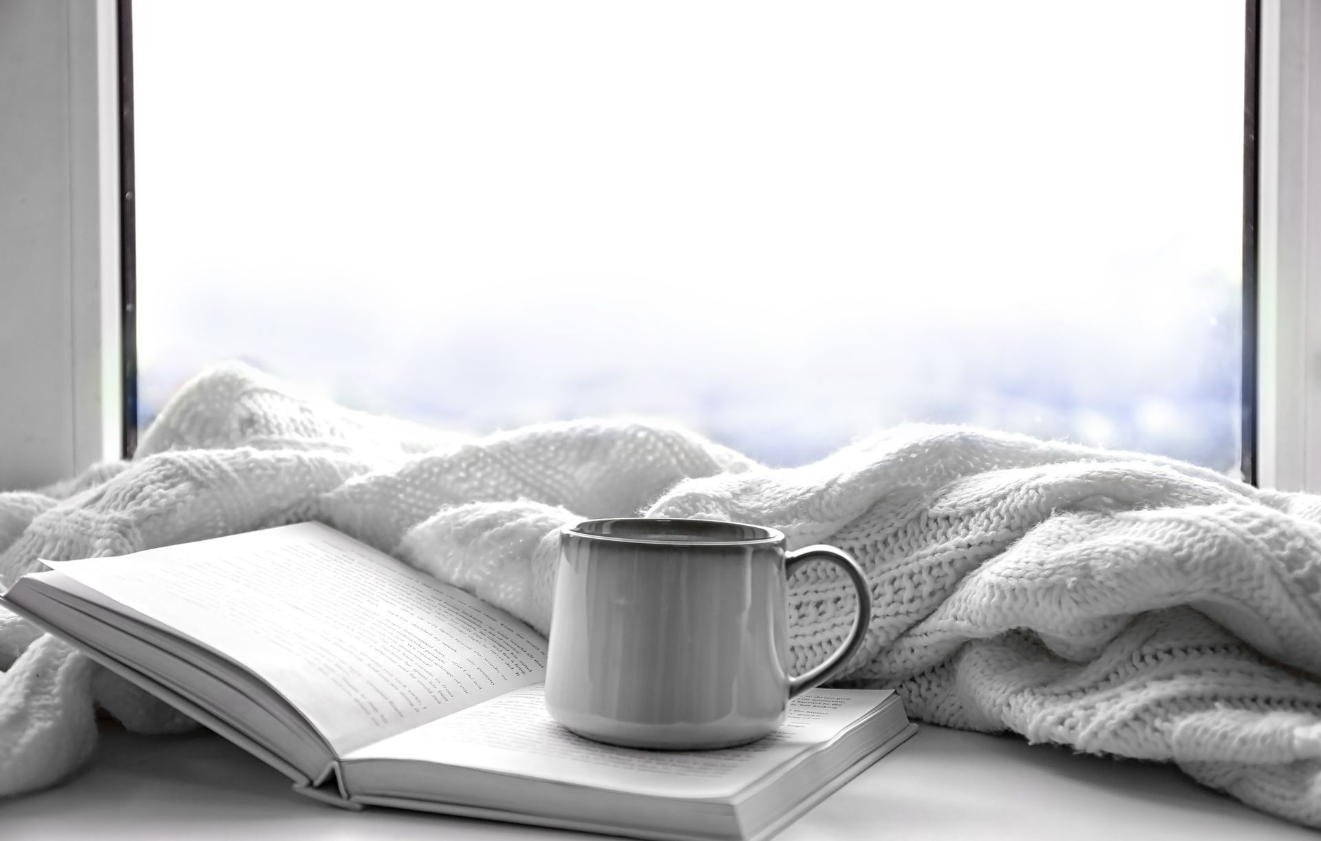 Rebord de fenêtre confortable avec un livre ouvert, une tasse blanche et une couverture tricotée dans la douce lumière du jour