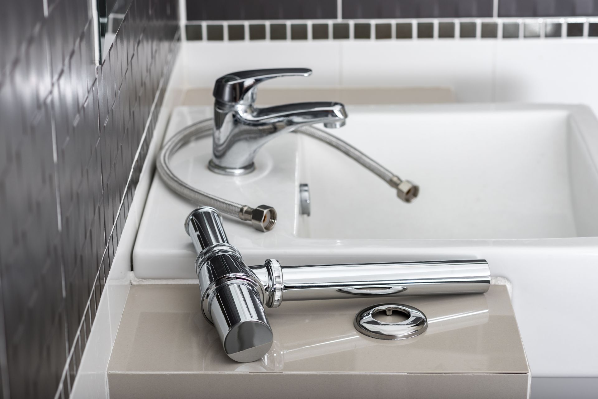 Robinet de salle de bains chromé à côté d'un lavabo avec douchette et bonde séparées, sur un comptoir beige