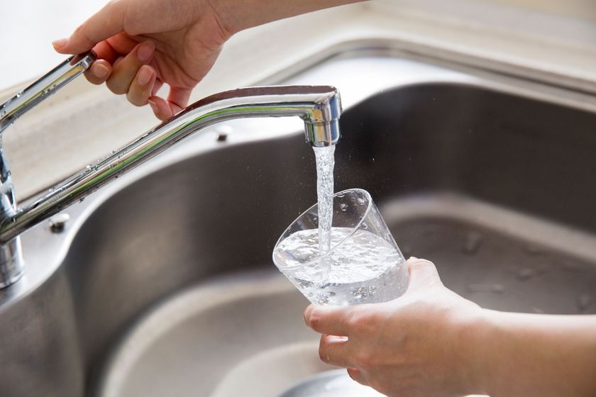 Des mains remplissent un verre d'eau au robinet de la cuisine, au-dessus de l'évier.