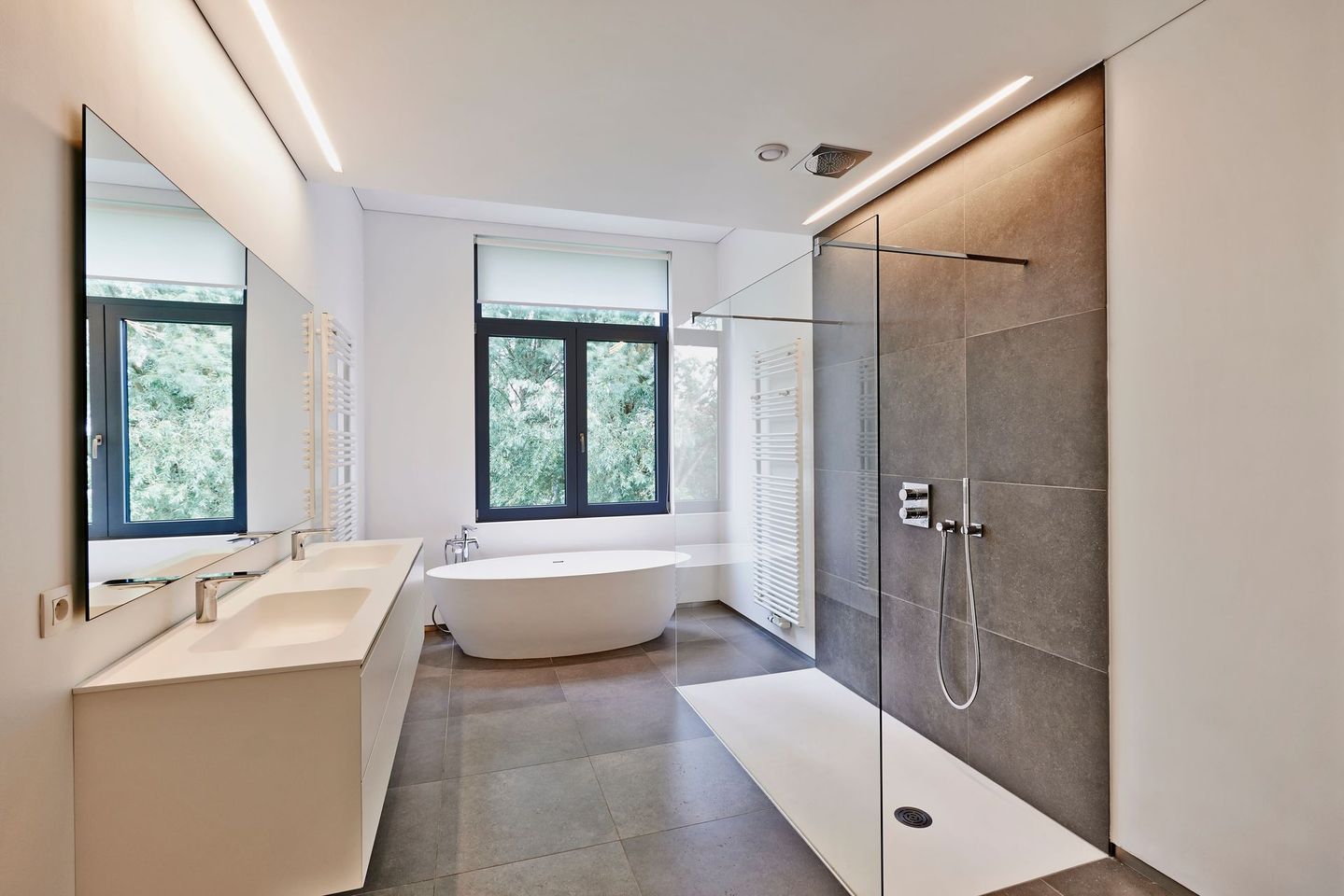 Salle de bains moderne avec meuble-lavabo en bois, miroir rond, douche, toilettes et sèche-serviettes mural.