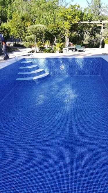 Una gran piscina azul con escaleras que conducen a ella rodeada de árboles.