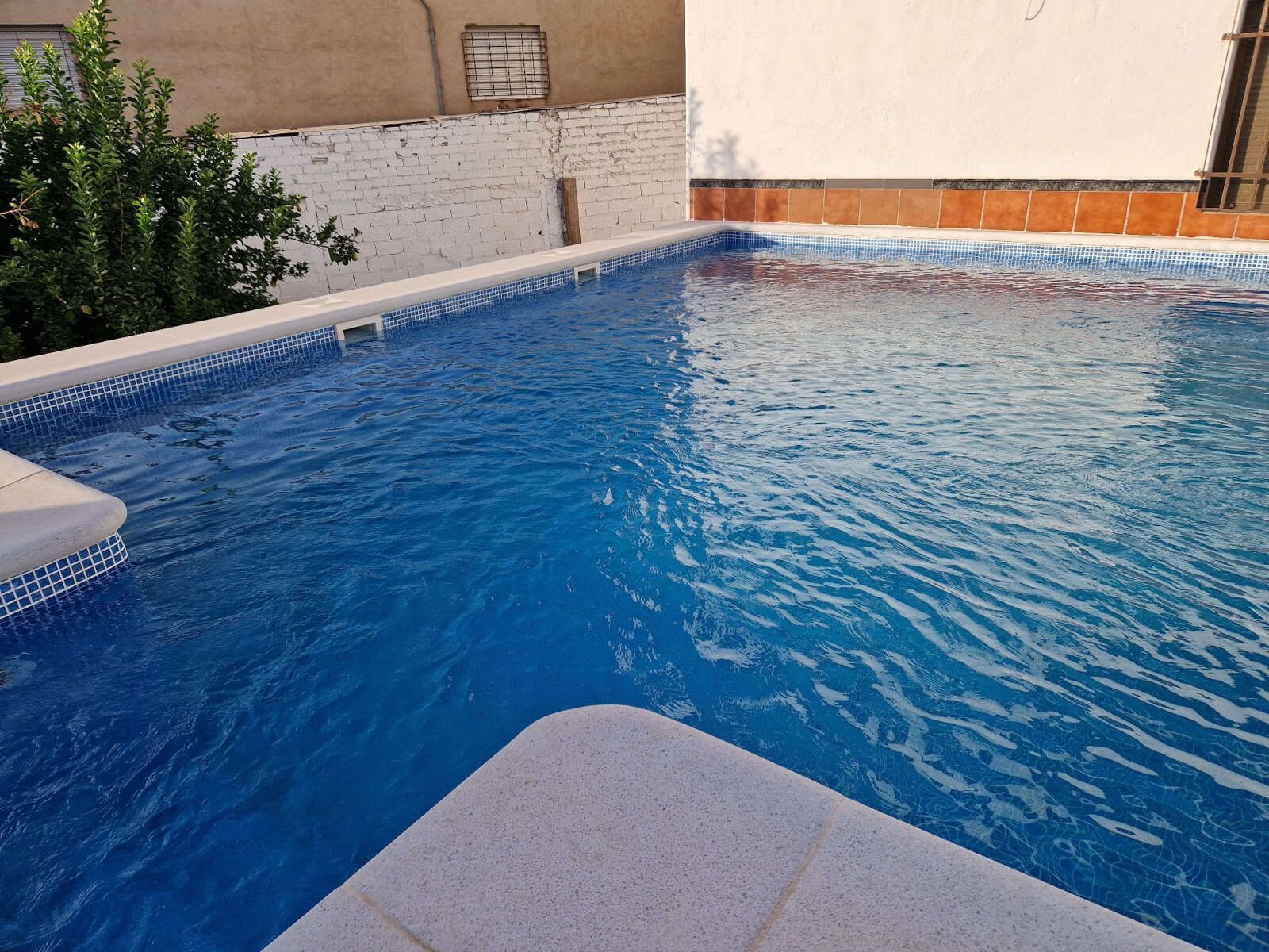 Una gran piscina con agua azul y borde blanco.