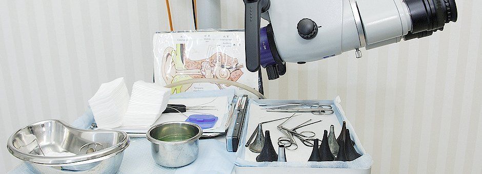 Un microscopio médico colocado sobre una bandeja con instrumental para exploración otorrinolaringológica, espéculos y gasas en un entorno clínico.