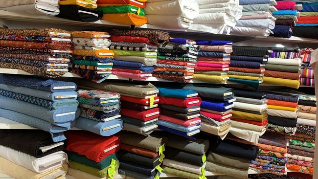 Étagères remplies de textiles de couture aux couleurs variées dans un magasin de tissus.