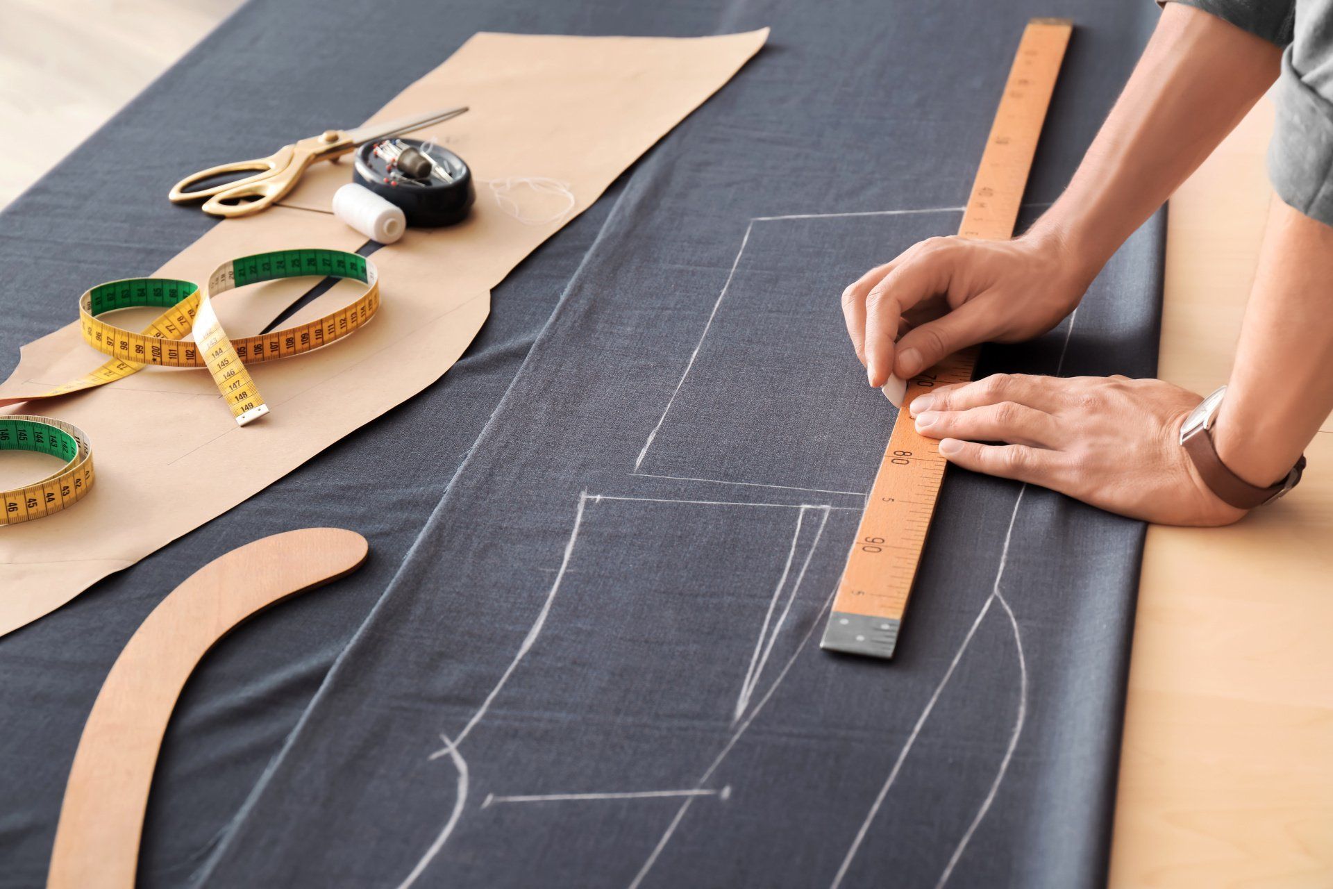 Traçage de patron sur un tissu gris. Une femme utilise une règle en bois pour effectuer les mesures.