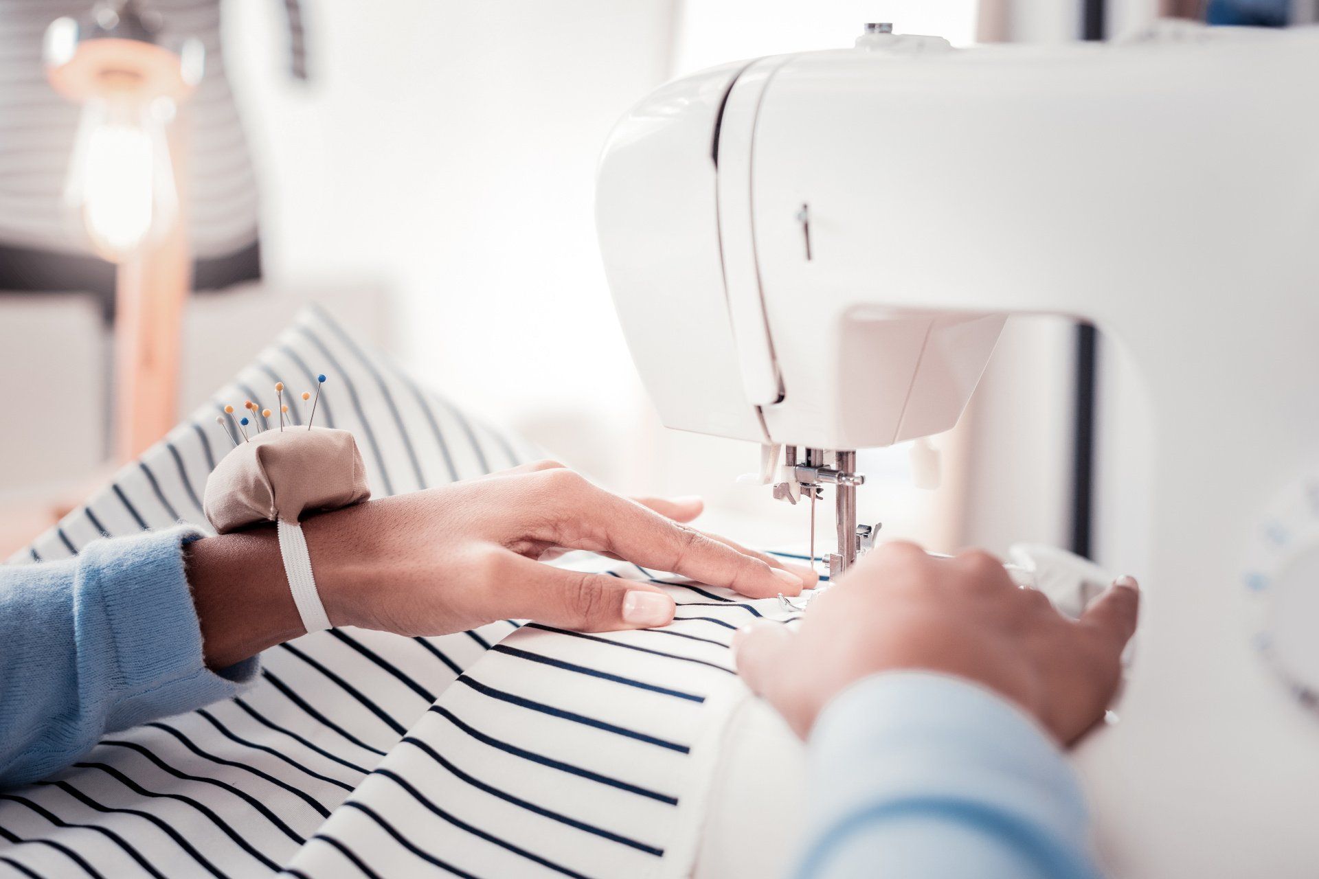 Des mains cousent un tissu rayé façon marinière à l'aide d'une machine à coudre.