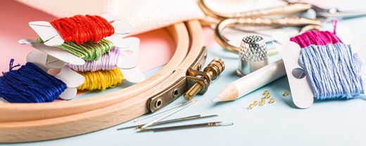 Accessoires de couture avec fils à broder colorés et tambour à broder sur un bureau bleu clair.