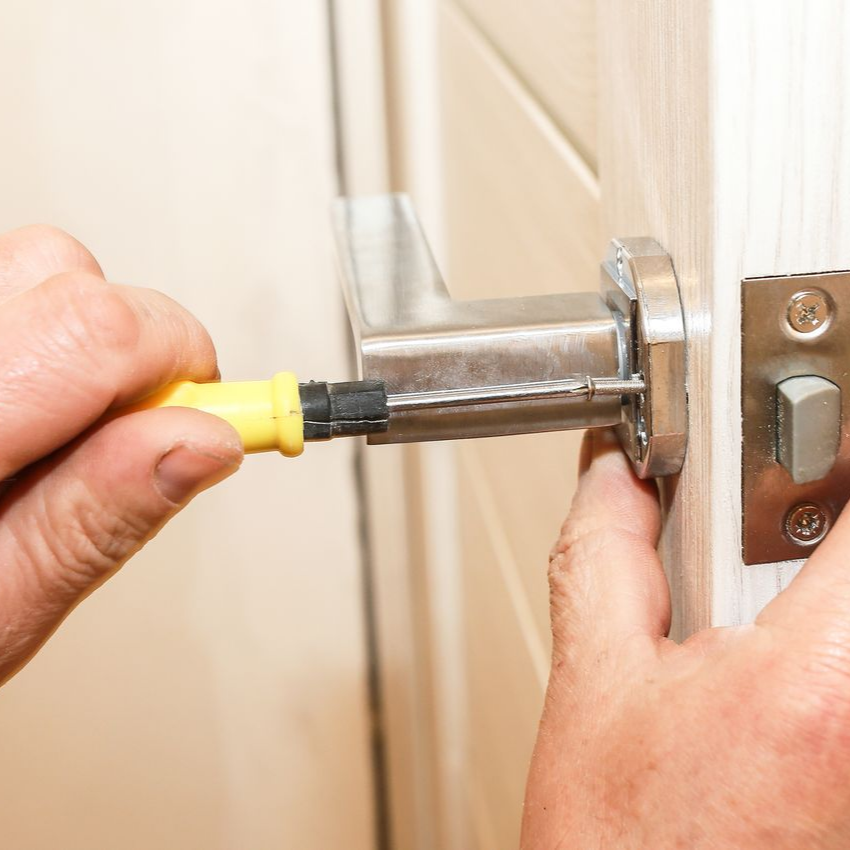 Personne utilisant un tournevis jaune pour installer une poignée de porte argentée sur une porte blanche.