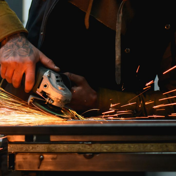 Une personne qui broie du métal, des étincelles jaillissent, à l'intérieur avec une action concentrée.