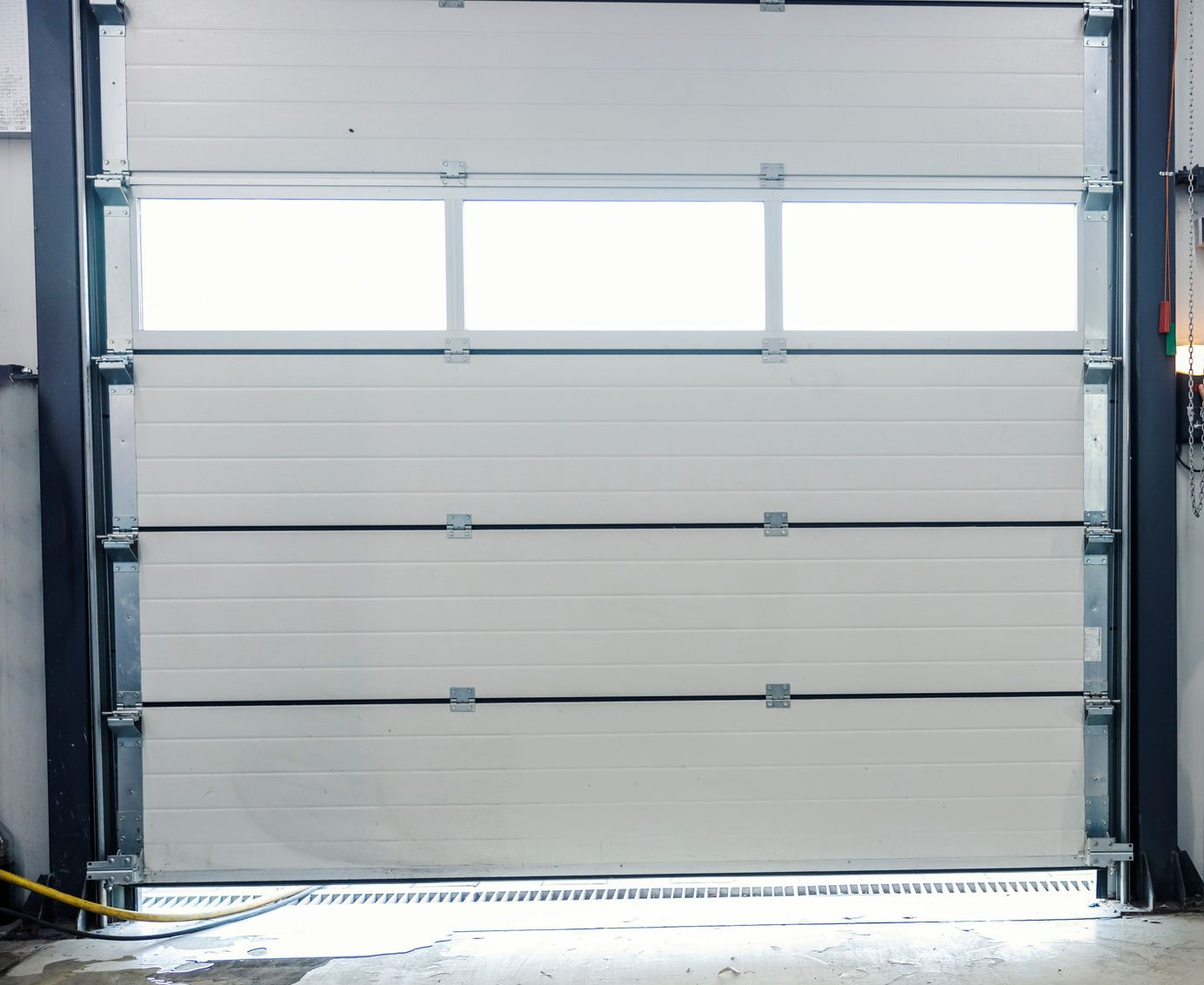Porte de garage industrielle blanche avec trois panneaux de fenêtre.