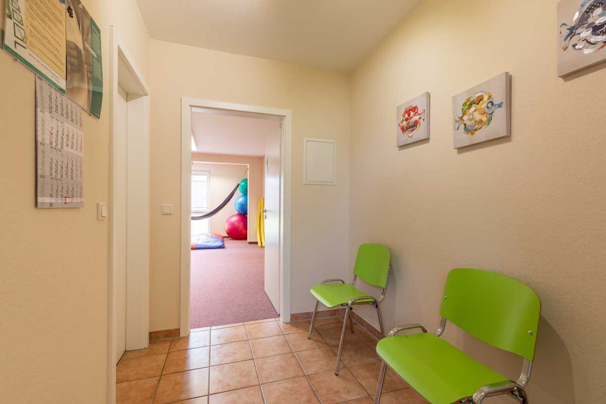 Ein Flur mit grünen Stühlen und einer Tür, die zu einem Zimmer führt.