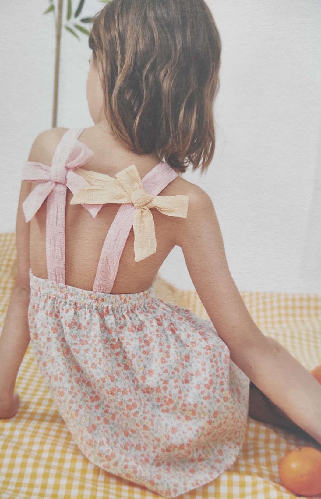 Una niña con un vestido floral está sentada sobre un mantel a cuadros.