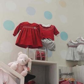 Un osito de peluche está sentado en un estante junto a una exhibición de ropa de bebé.