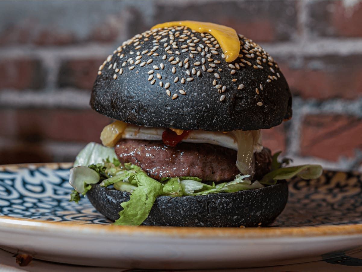 Una hamburguesa negra con queso y lechuga en un plato.
