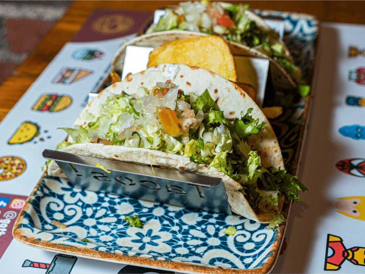 Tres tacos están sentados en un plato colorido sobre una mesa.
