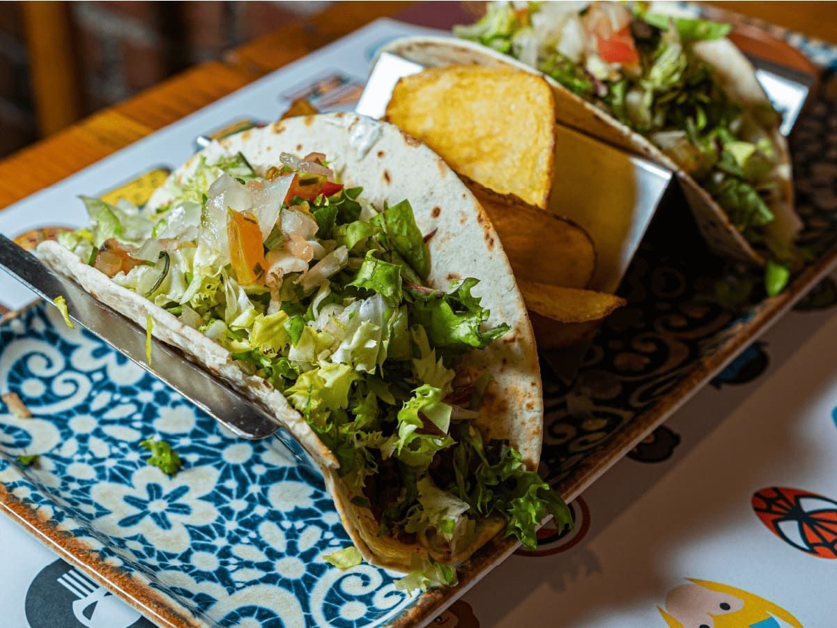Un primer plano de un plato de comida con tacos y patatas fritas en una mesa.