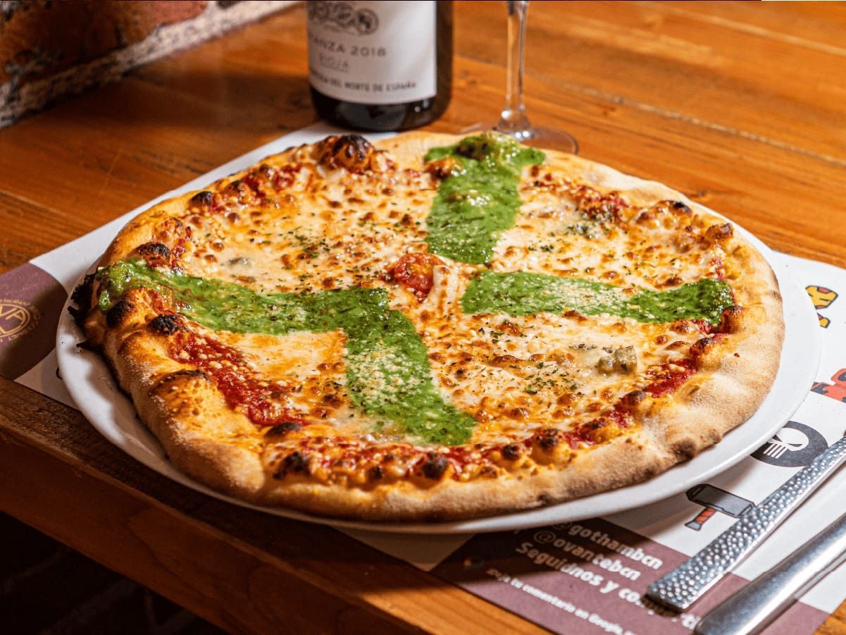 Una pizza con una cruz está en un plato sobre una mesa al lado de una botella de vino.