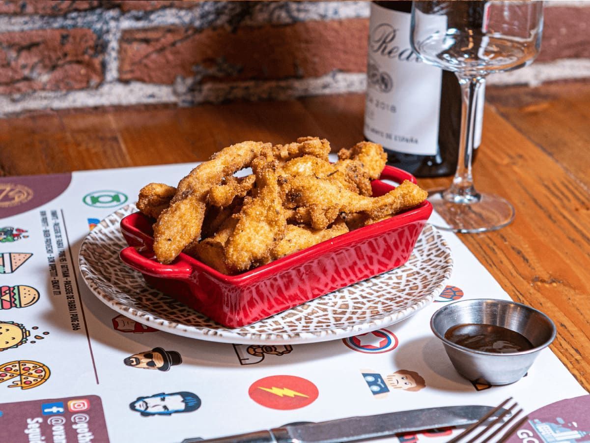 Un plato de pollo frito en una mesa junto a una botella de vino.