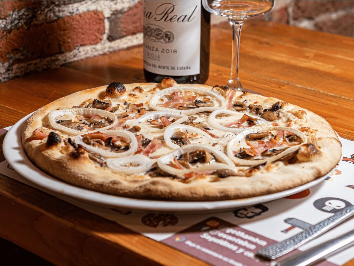 Una pizza está en un plato al lado de una botella de vino.