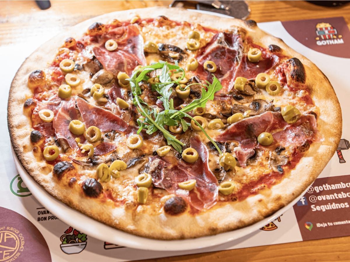 Una pizza con aceitunas, jamón y champiñones en un plato sobre una mesa.