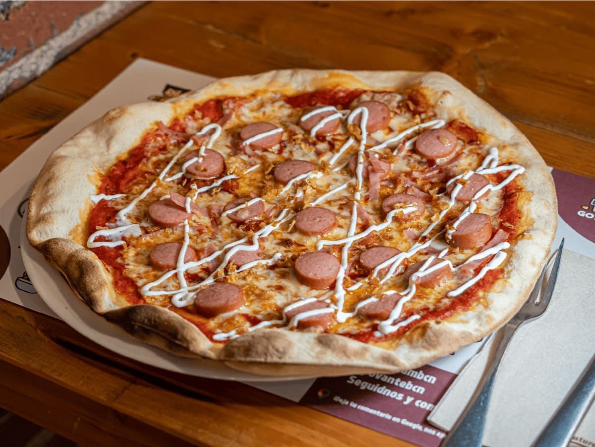 Una pizza con salchicha y queso está sentada sobre una mesa con un tenedor.
