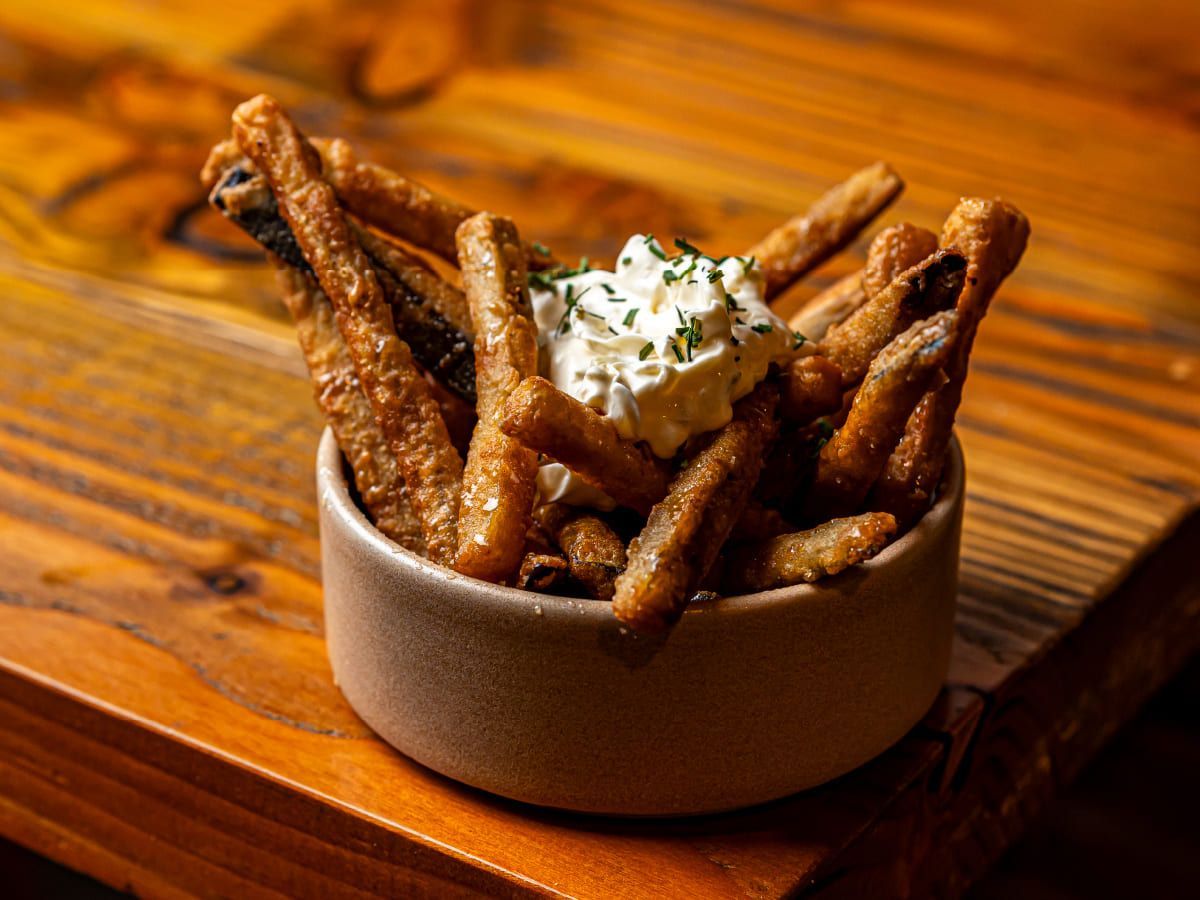 Un tazón de papas fritas con crema agria sobre una mesa de madera.