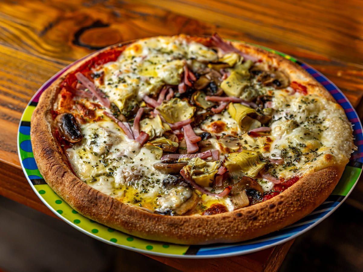 Una pizza está colocada en un plato colorido sobre una mesa de madera.