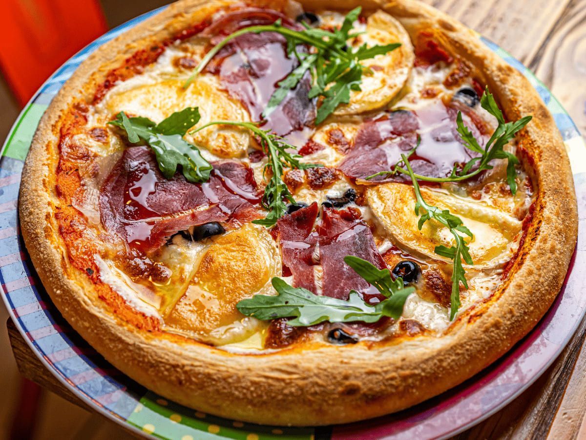Una pizza está colocada en un plato colorido sobre una mesa de madera.