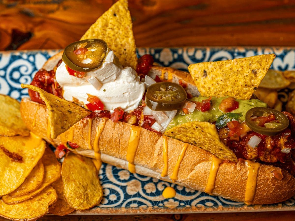 Un chili dog con guacamole, crema agria, jalapeños y papas fritas en un plato.