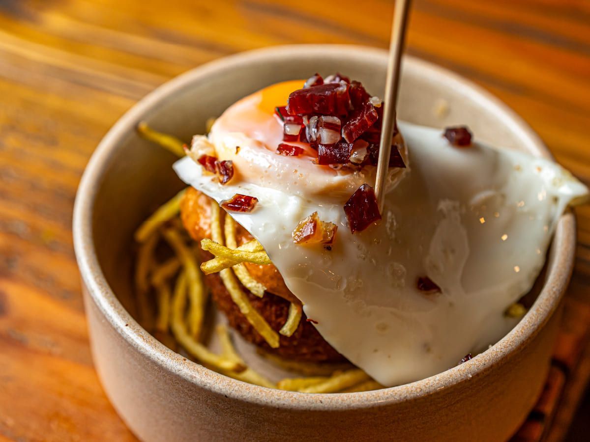 Un plato de comida con un huevo frito y patatas fritas sobre una mesa de madera.