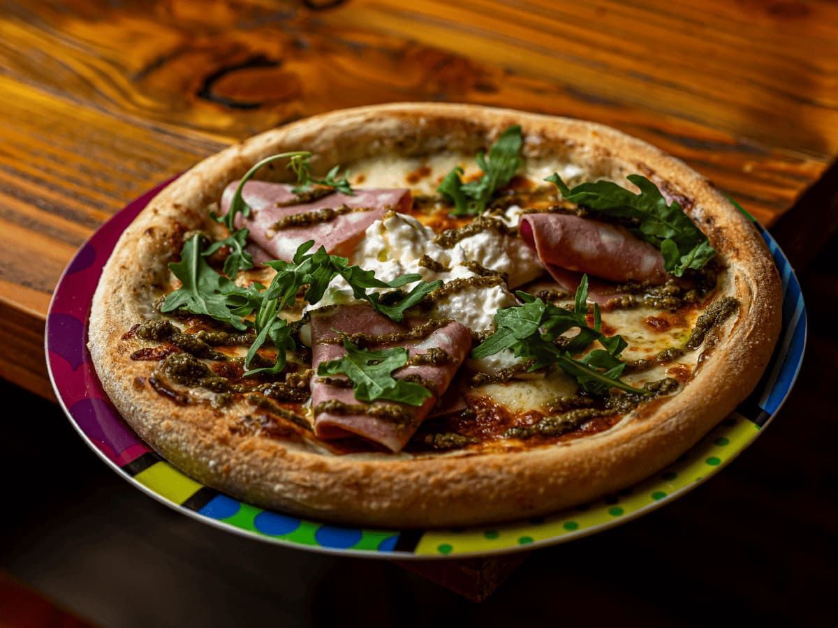 Una pizza está colocada en un plato colorido sobre una mesa de madera.