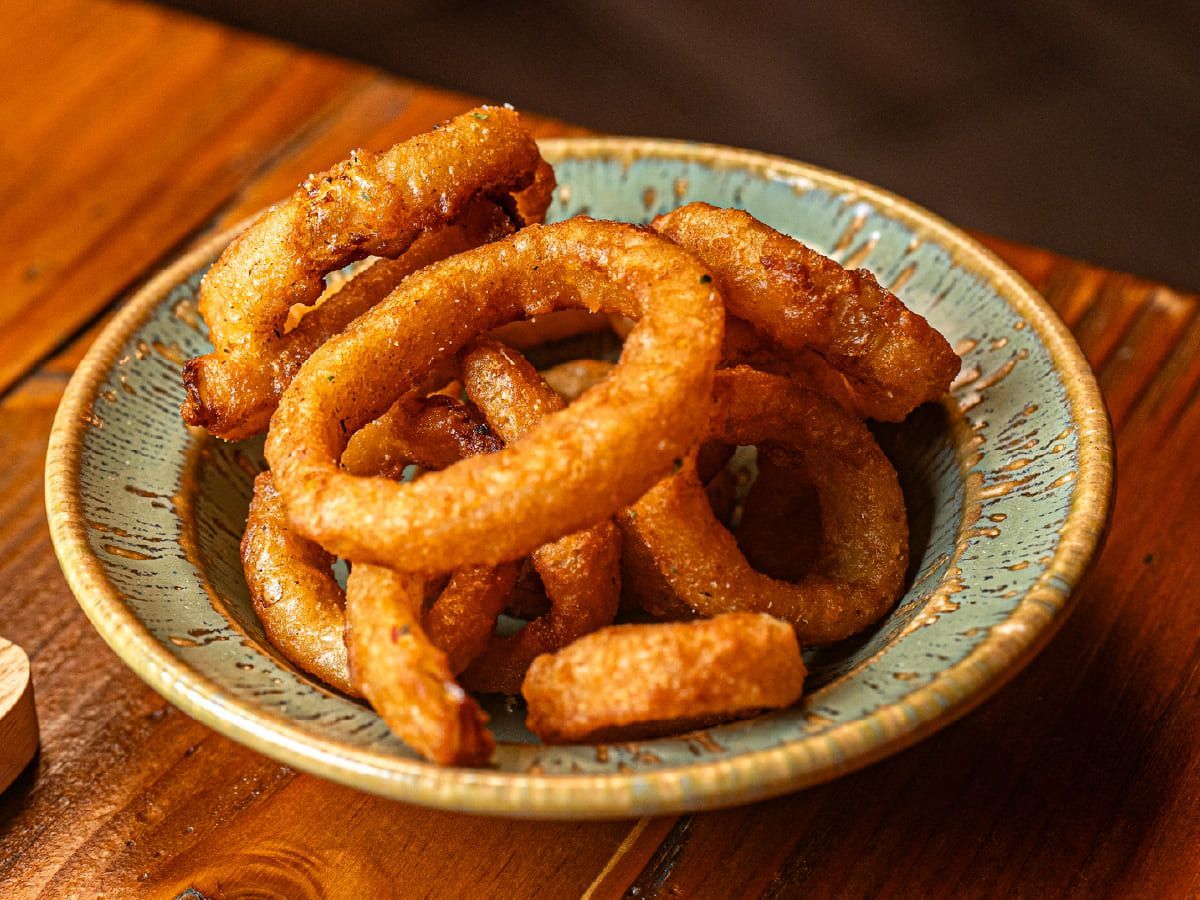 Un bol de aros de cebolla está sobre una mesa de madera.