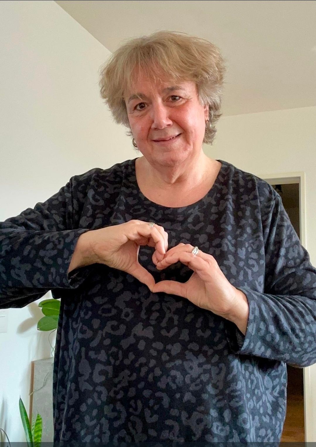 Eine Person mit kurzen, hellen Haaren, die ein dunkles, langärmeliges Hemd mit Tiermuster trägt.