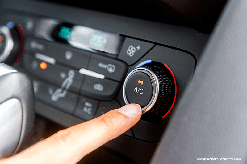 Ein Finger drückt den Klimaanlagenknopf (A/C) auf dem Klimabedienteil des Autos.