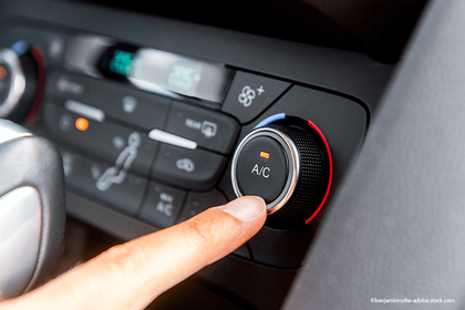 Ein Finger drückt den Klimaanlagenknopf (A/C) auf dem Klimabedienteil des Autos.